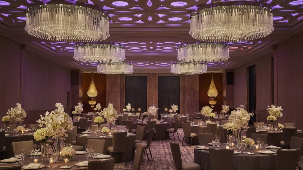 This elegant indoor wedding venue in Casablanca showcases luxurious chandeliers, warm lighting, and perfectly arranged tables, ideal for creating a memorable celebration while managing your wedding costs.